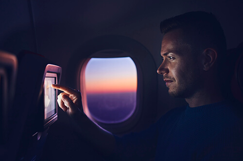 Man travel by airplane during night. Passenger using in-flight entertainment system and internet connection.