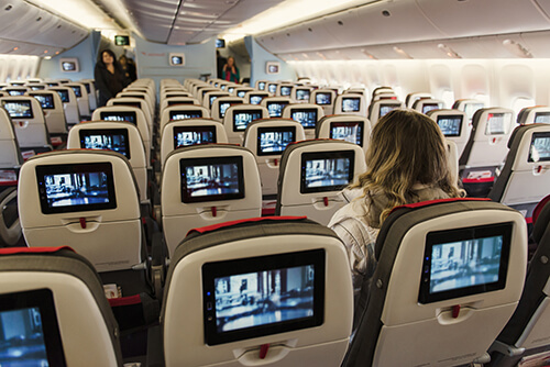 Seats on board of airplane. Cabin of economy class with tv screens and first passengers.